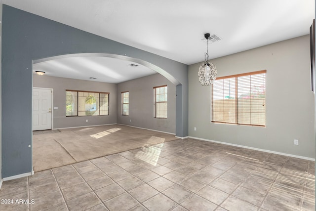 carpeted spare room with an inviting chandelier and a wealth of natural light