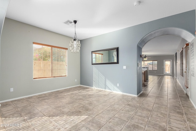 spare room featuring ceiling fan with notable chandelier and light tile patterned floors