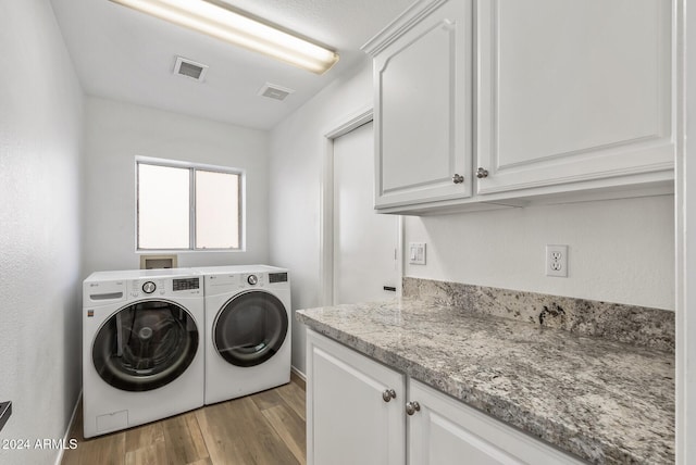 laundry room featuring separate washer and dryer, light hardwood / wood-style flooring, and cabinets