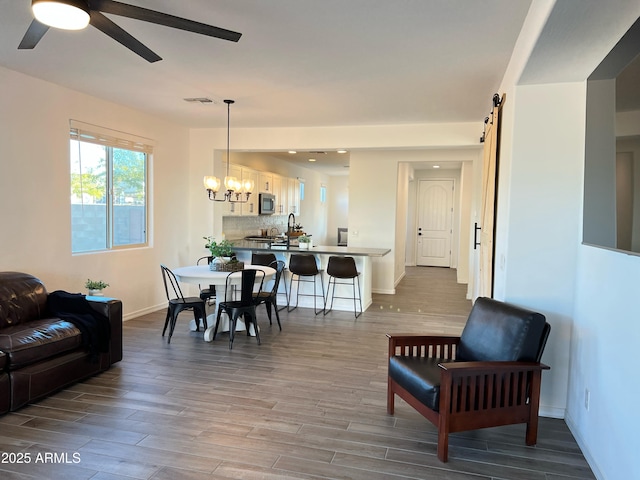 living room featuring ceiling fan with notable chandelier, wood-type flooring, and a barn door