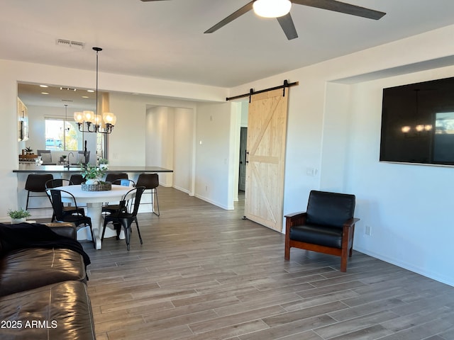 dining area featuring ceiling fan with notable chandelier, wood-type flooring, and a barn door