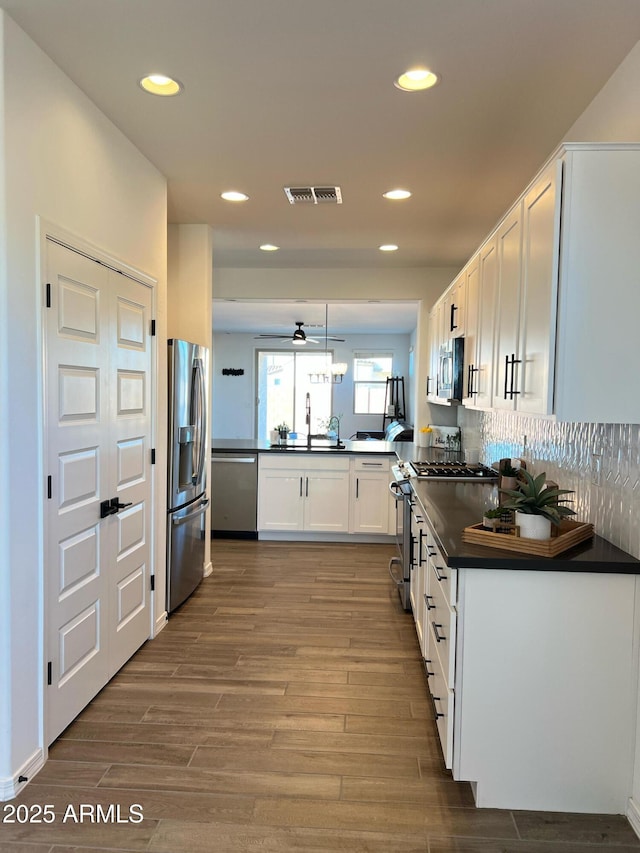 kitchen with wood-type flooring, kitchen peninsula, sink, white cabinetry, and stainless steel appliances