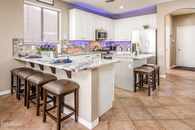 kitchen featuring a breakfast bar, a center island, appliances with stainless steel finishes, light stone counters, and white cabinetry