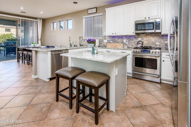 kitchen featuring a center island, light stone counters, a breakfast bar, white cabinets, and appliances with stainless steel finishes