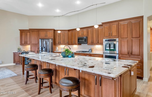 kitchen featuring hanging light fixtures, a spacious island, a kitchen bar, appliances with stainless steel finishes, and light wood-type flooring