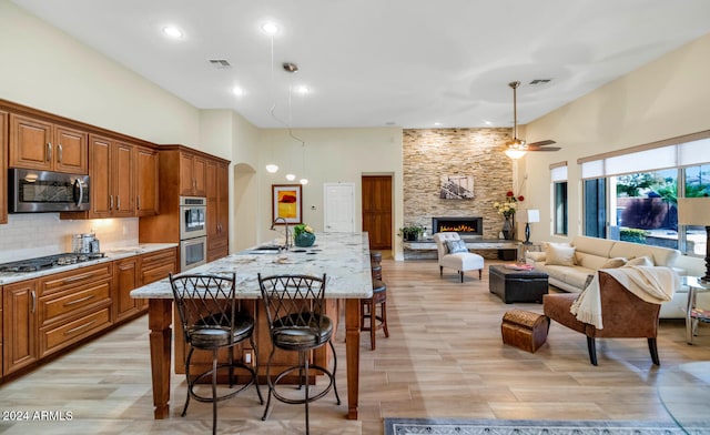 kitchen featuring a breakfast bar, a center island with sink, a stone fireplace, sink, and stainless steel appliances