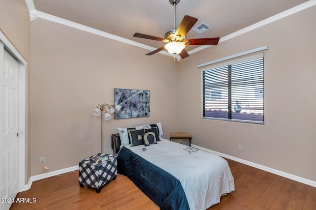 bedroom with ceiling fan, wood-type flooring, ornamental molding, and a closet