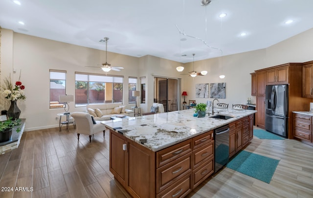 kitchen featuring a kitchen island with sink, sink, light stone countertops, light hardwood / wood-style floors, and stainless steel appliances