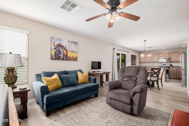 living room featuring ceiling fan with notable chandelier and light wood-type flooring