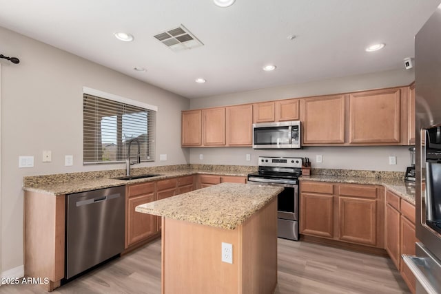 kitchen featuring appliances with stainless steel finishes, light hardwood / wood-style floors, light stone counters, a kitchen island, and sink