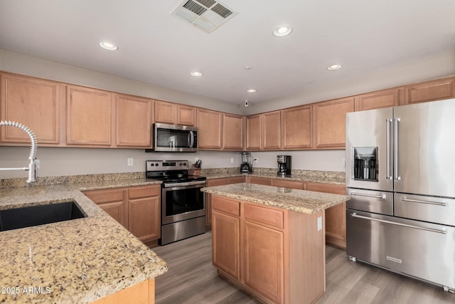 kitchen featuring appliances with stainless steel finishes, light hardwood / wood-style floors, light stone countertops, and a kitchen island