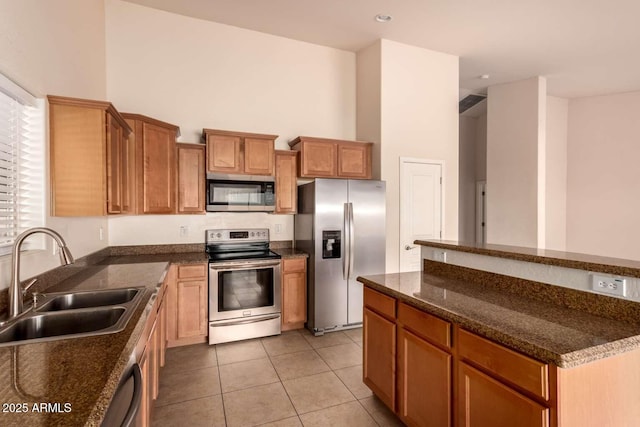 kitchen with a high ceiling, stainless steel appliances, dark stone counters, sink, and light tile patterned floors