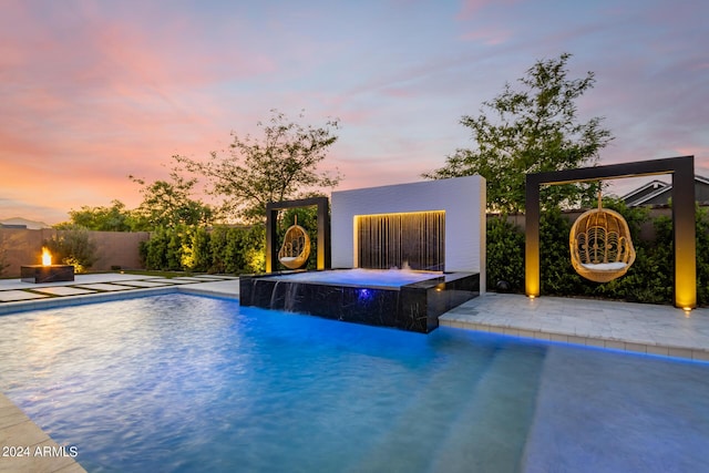 pool at dusk with pool water feature, a patio, and a fire pit