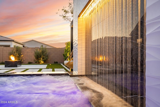 pool at dusk featuring a patio area, a hot tub, and an outdoor fire pit