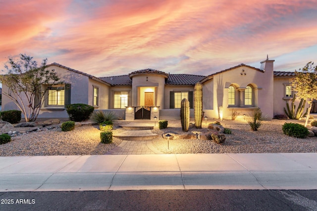 mediterranean / spanish-style home featuring a tile roof, a chimney, and stucco siding