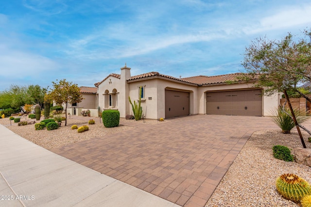 mediterranean / spanish house featuring stucco siding, a tile roof, decorative driveway, and a garage
