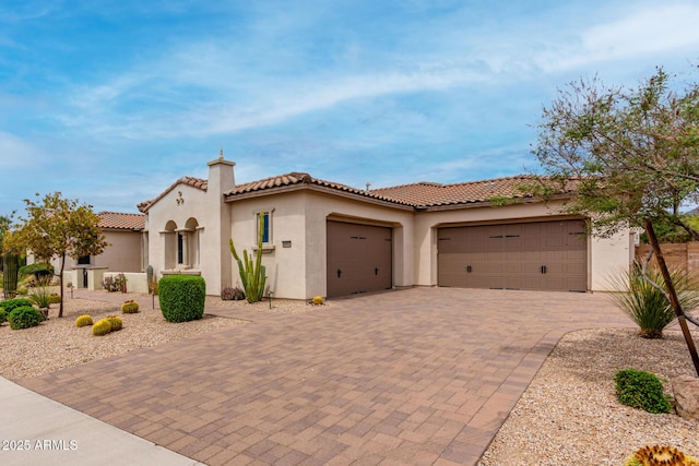 mediterranean / spanish house featuring stucco siding, an attached garage, decorative driveway, and a tiled roof