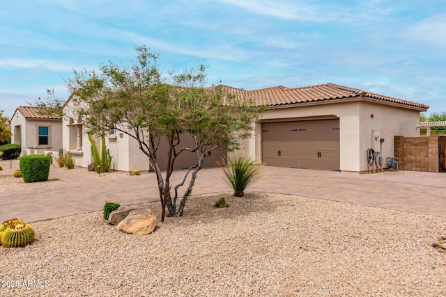 mediterranean / spanish-style house featuring decorative driveway, a tiled roof, fence, a garage, and stucco siding