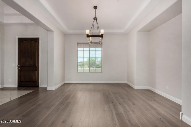 interior space with wood-type flooring, baseboards, an inviting chandelier, and a raised ceiling