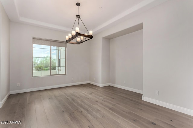 unfurnished room featuring baseboards, wood finished floors, an inviting chandelier, and a tray ceiling