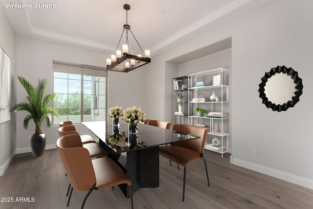 dining area with a raised ceiling, wood finished floors, baseboards, and a notable chandelier