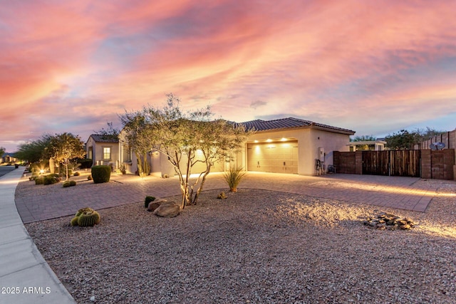 view of front of house with a tiled roof, driveway, fence, an attached garage, and stucco siding