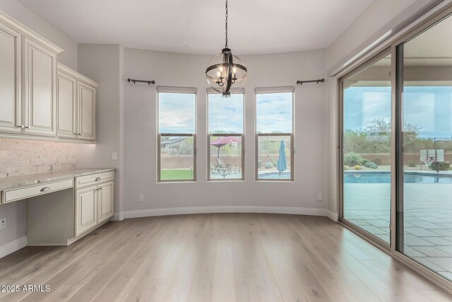 unfurnished dining area with light wood-style flooring, baseboards, and an inviting chandelier