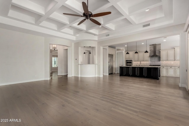 unfurnished living room with ceiling fan with notable chandelier, wood finished floors, visible vents, and coffered ceiling
