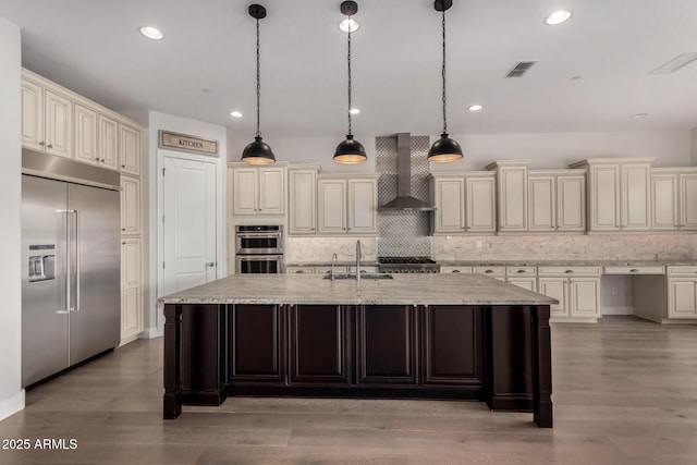 kitchen featuring a sink, stainless steel appliances, backsplash, wall chimney exhaust hood, and visible vents