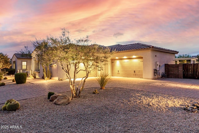 view of front facade featuring fence, stucco siding, a tile roof, driveway, and a garage