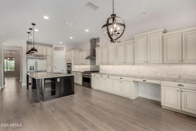 kitchen with wall chimney range hood, a notable chandelier, high end appliances, and cream cabinetry