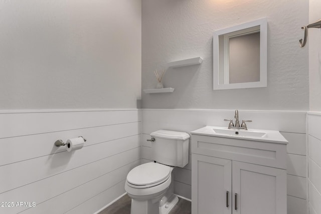 bathroom featuring vanity, toilet, and a wainscoted wall