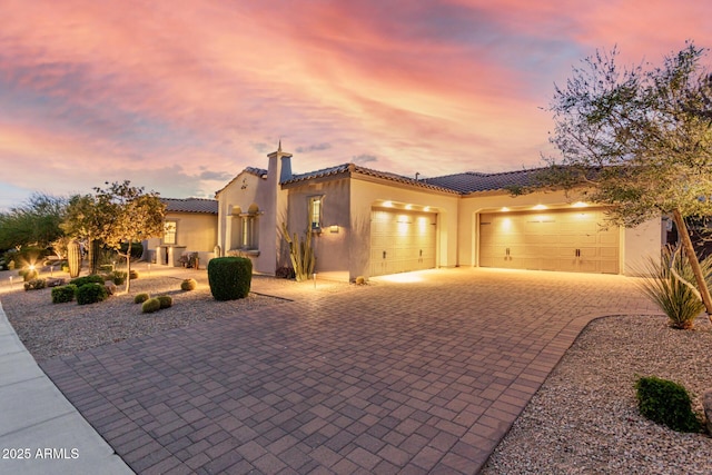 mediterranean / spanish home featuring stucco siding, an attached garage, decorative driveway, and a tiled roof