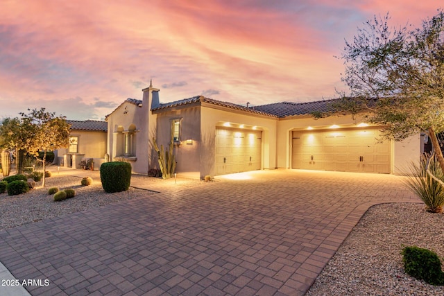 view of front of property with stucco siding, an attached garage, a tiled roof, and decorative driveway