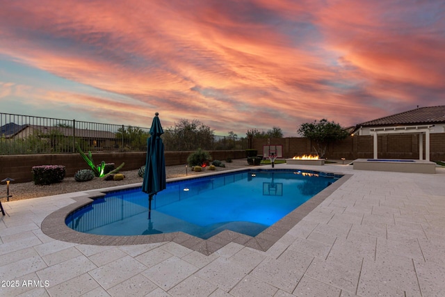 pool at dusk with a patio, a fenced in pool, a fenced backyard, an in ground hot tub, and an outdoor fire pit