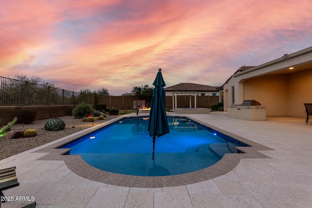 pool at dusk featuring a fenced in pool, a patio area, an outdoor kitchen, and a fenced backyard