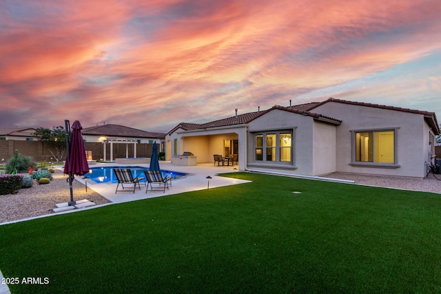 back of property at dusk featuring a lawn, a tiled roof, a fenced backyard, a fenced in pool, and stucco siding