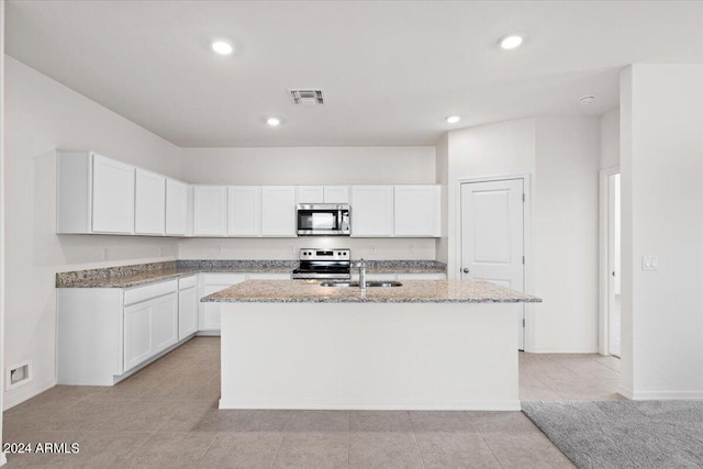 kitchen with white cabinets, light stone counters, stainless steel appliances, and a kitchen island with sink