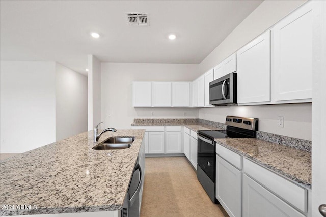 kitchen with light stone countertops, sink, white cabinetry, stainless steel appliances, and a kitchen island with sink