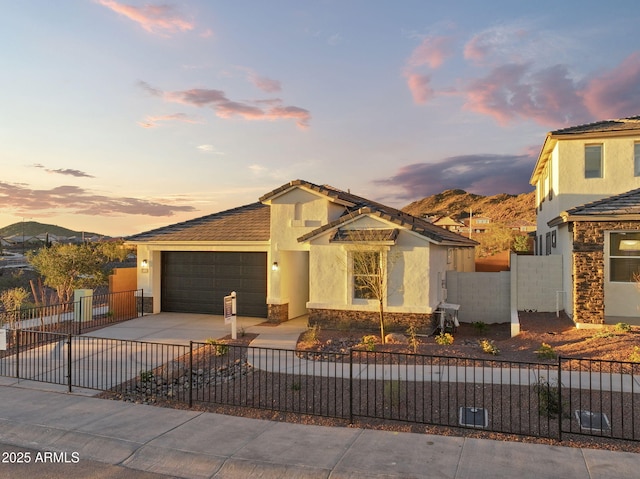 view of front of home featuring a fenced front yard, stucco siding, an attached garage, stone siding, and driveway