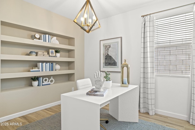 home office featuring light wood finished floors, a notable chandelier, baseboards, and built in features