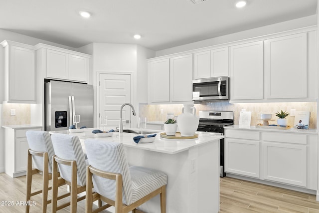 kitchen with stainless steel appliances, white cabinets, a center island with sink, and decorative backsplash