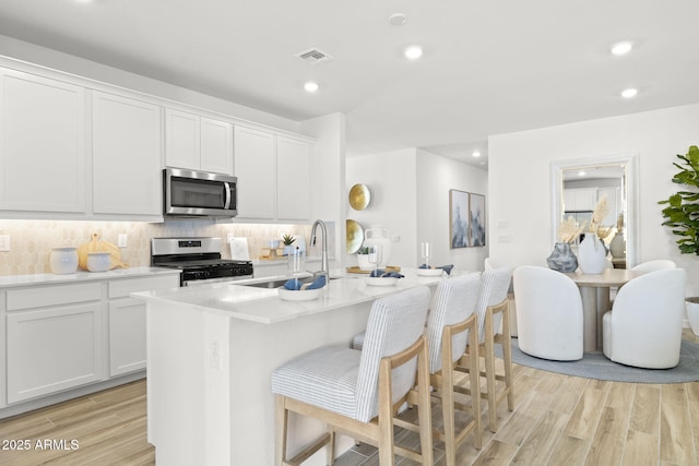 kitchen with light wood-style flooring, stainless steel appliances, a sink, white cabinetry, and tasteful backsplash