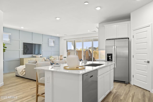 kitchen with light wood-style flooring, appliances with stainless steel finishes, white cabinets, a sink, and an island with sink