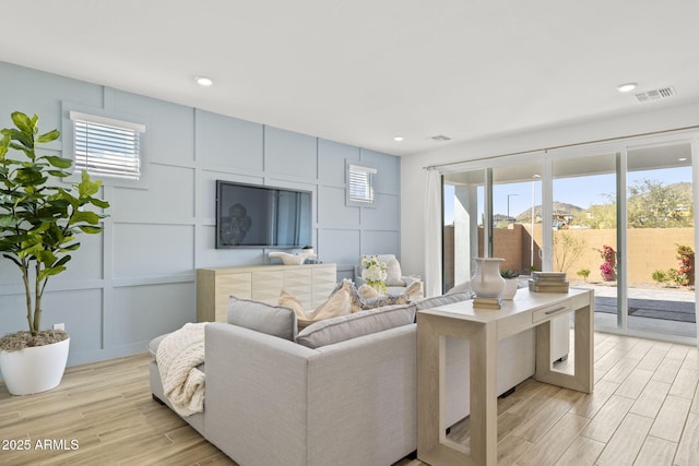 living area with light wood-style floors, visible vents, a decorative wall, and recessed lighting