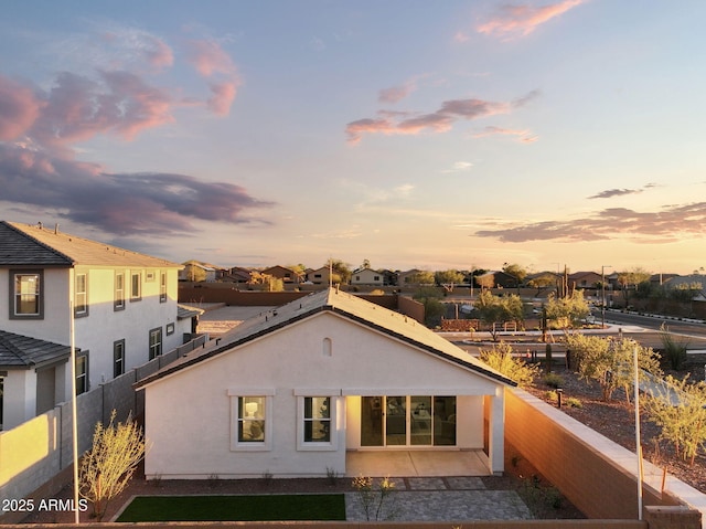 back of property at dusk with a residential view, fence, and stucco siding