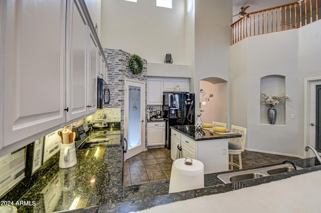 kitchen with black appliances, a towering ceiling, white cabinetry, decorative backsplash, and sink