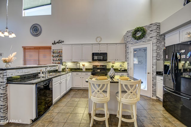 kitchen with hanging light fixtures, white cabinets, tasteful backsplash, a towering ceiling, and black appliances