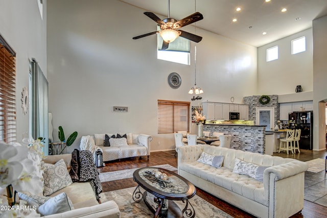 living room with wood-type flooring, ceiling fan with notable chandelier, and a high ceiling