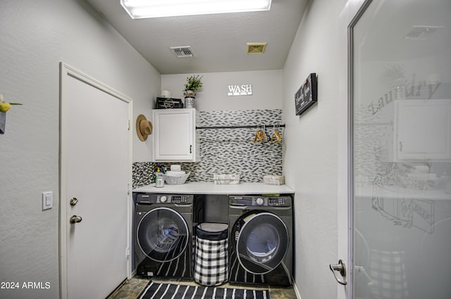 laundry room featuring washing machine and clothes dryer, a textured ceiling, and cabinets